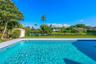 In-ground swimming pool with light-colored coping, surrounded by a paved deck, green lawn, and mature perimeter landscaping