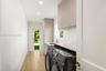 Laundry area featuring minimalist flat-panel cabinetry, light-toned stone-finish countertops, an undermount sink with a gooseneck faucet, wood-finish 