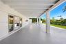 Covered rear patio featuring a white-painted exposed beam ceiling, large-format tile flooring, and multiple sliding glass door entries