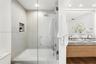 Shower and tub combination featuring glass enclosure, rain-style shower head, built-in recessed wall niche, dual-sink vanity with stone-finish counter