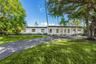 Single-story exterior featuring a covered front porch with white columns, paved driveway, and mature landscaping