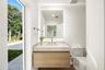 Floating wood-finish vanity with a stone countertop, rectangular undermount sink, integrated backlit mirror, and dual-flush toilet
