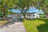 Single-story exterior featuring white masonry walls, a flat roofline, paved driveway, and mature landscaping