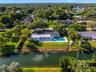 Waterfront residence featuring a rectangular swimming pool, covered patio, sprawling lawn, and mature trees