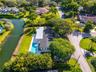 Aerial perspective of residential property featuring a swimming pool, concrete patio, asphalt shingle roofing, and expansive green space with mature t