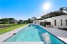 Rectangular in-ground swimming pool with mosaic tile border, light-toned stone pool deck, and manicured grass grounds