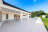Covered patio featuring an expansive concrete surface, support columns, sliding glass doors, a built-in swimming pool, and a manicured lawn