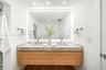 Floating wood-finish vanity with dual integrated sinks, stone-surface countertop, LED-backlit mirror, and wall-mounted metal fixtures