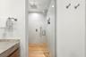 Walk-in shower featuring glass enclosure, ceiling-mounted rainfall showerhead, handheld sprayer, integrated wall niche, and wood-finish flooring