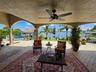 Covered lanai featuring arched columns, paved flooring, and a ceiling fan, overlooking a pool and waterfront