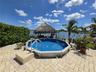 Above-ground pool with a surrounding paved patio, thatched-roof cabana, and waterfront bulkhead