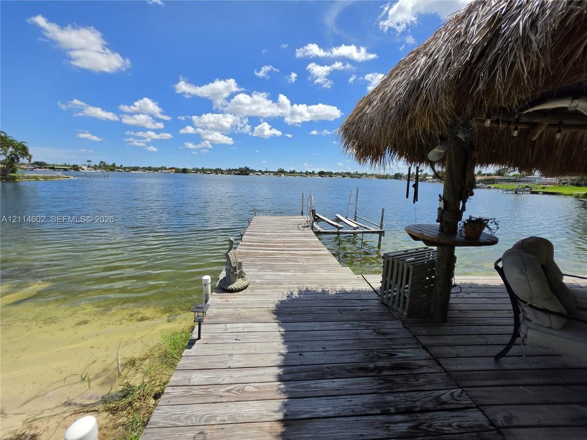 Waterfront property featuring a wooden dock, a thatch-roofed gazebo, and a built-in boat lift