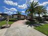 Exterior facade featuring stone veneer detailing, expansive paver driveway, manicured landscaping, mature palm trees, and decorative wall accents