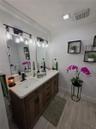 Double vanity featuring a light-toned countertop, dual rectangular undermount sinks, wood-finish cabinetry, matte black hardware, and two industrial-s