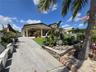 Covered patio featuring architectural pillars, concrete driveway, stone-finished retaining wall, and landscaped lawn