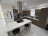 Kitchen featuring a central island with a quartz countertop and integrated cooktop, stainless steel chimney-style range hood, wood-finish cabinetry, s