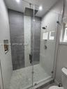 Walk-in shower featuring a frameless glass enclosure, ceiling-mounted rainfall showerhead, pebble stone floor, vertical mosaic tile accent, and a buil