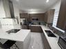 Kitchen featuring wood-finish cabinetry, quartz countertops, a central island with a built-in cooktop, stainless steel chimney-style range hood, and t