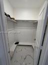 Walk-in storage space featuring white built-in shelving, integrated hanging rods, and large-format porcelain tile flooring with marble-finish veining