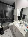Bathroom featuring a glass-enclosed shower with tile surround, white cabinetry, integrated sink with stone-finish countertop, and large-format porcela