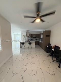 Large-format tile flooring with veining detail, central island with seating, stainless steel range hood, built-in cabinetry, and ceiling-mounted light
