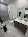 Bathroom featuring a large-format tiled floor, a vanity with a light-toned countertop, and a walk-in shower enclosed by a frameless glass door with fl