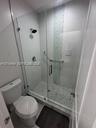 Walk-in shower featuring a frameless glass enclosure, pebble-stone flooring, a decorative vertical glass tile accent, and a wall-mounted showerhead