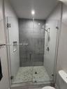 Walk-in shower featuring a glass enclosure, gray tile surround, pebble-style floor, built-in recessed niche, and handheld shower fixture