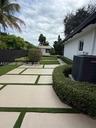 Backyard featuring large-format paver hardscaping with turf ribbons, perimeter privacy fencing, manicured hedges, and an external storage structure