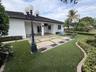 Covered concrete patio with geometric inlay, manicured lawn, established shrubbery, and multi-globe ornamental lamp posts