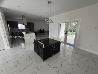 Polished stone-finish tile flooring, kitchen island with built-in cabinetry, stainless steel range hood, recessed lighting, and double glass pane door