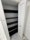 Storage closet featuring white paneled swing doors, multiple horizontal shelving tiers with dark-toned surfaces, and large-format tile flooring with v