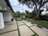 Backyard featuring large-format paver hardscaping with turf ribbons, mature specimen trees, sculpted landscaping, and wall-mounted exterior globe ligh