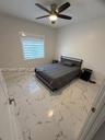 Large-format tile flooring with veined detailing, neutral wall tones, multi-blade ceiling fan with integrated lighting, and horizontal shade window tr