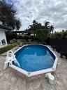 Oval swimming pool with tile-surfaced exterior, stone-paver decking, and a covered outdoor structure featuring built-in masonry elements