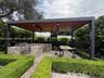 Outdoor kitchen featuring a stone-clad island, stainless steel grill, built-in refrigerator, and stone-topped bar under a covered pergola with integra