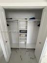 Walk-in closet featuring white-finish built-in shelving, two overhead storage ledges, metal hanging rods, and large-format tile flooring with a veined