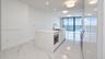 Kitchen featuring a central island with a quartz countertop, integrated microwave, undermount stainless steel sink, sleek high-gloss cabinetry, and li