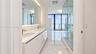 Bathroom featuring white cabinetry, dual undermount sinks with brass-tone fixtures, wall-to-wall mirror, large-format tile flooring, and a glass-enclo