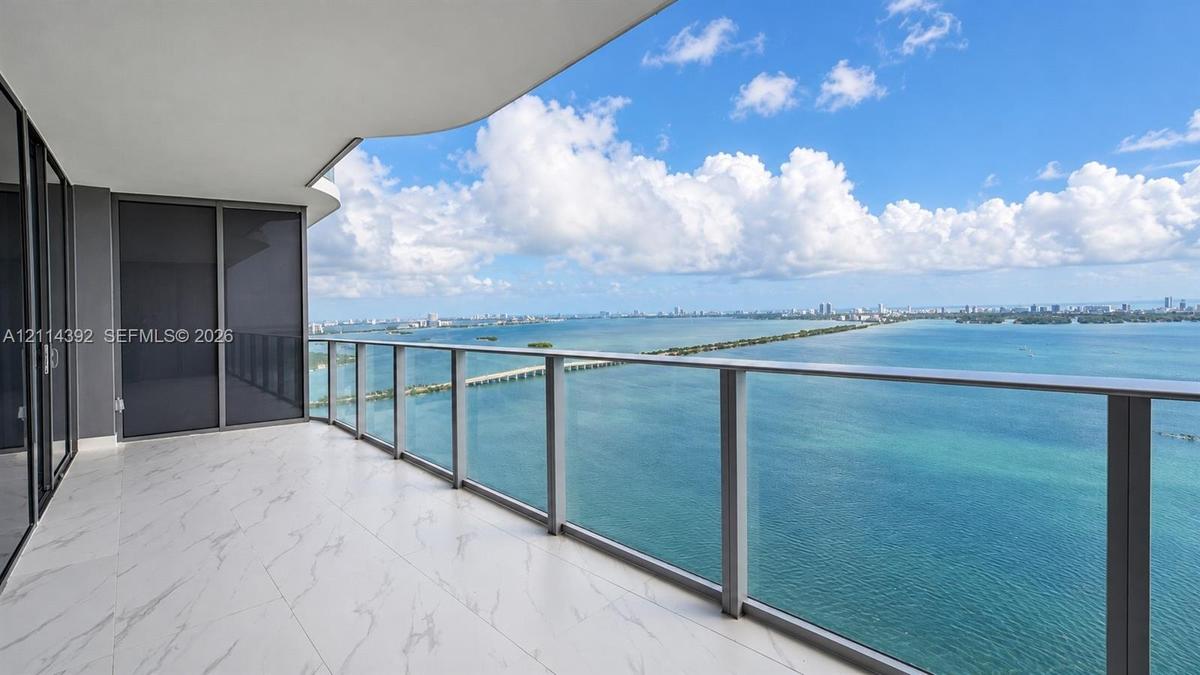 Expansive covered balcony featuring large-format stone-look tile flooring, a sleek glass railing system, and full-height glass panel doors