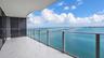 Expansive covered balcony featuring large-format stone-look tile flooring, a sleek glass railing system, and full-height glass panel doors