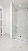 Walk-in shower featuring glass enclosure, wall-mounted rainfall showerhead, and large-format tile flooring and wall surfacing with veined detailing