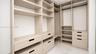 Custom walk-in closet featuring extensive built-in shelving, multiple integrated drawers with matte black pulls, dual hanging rods, and stone-finish f