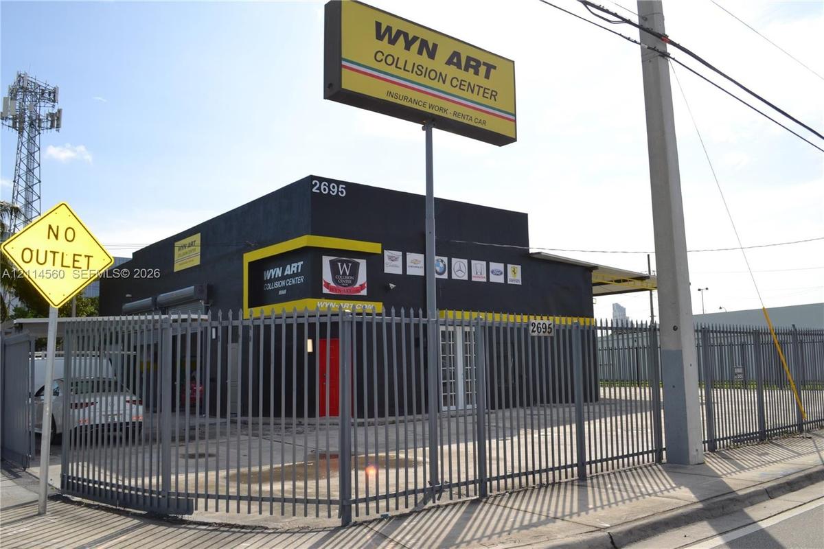 Commercial property featuring a concrete masonry structure, metal-slat security fencing, and an integrated overhead roll-up door