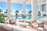 Covered terrace featuring natural stone flooring, oversized structural support columns, and access to an expansive outdoor pool with built-in planter