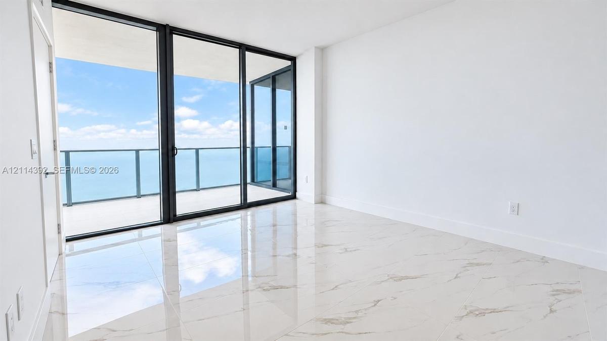 Floor-to-ceiling sliding glass doors, oversized tile flooring, and a glass-paneled balcony