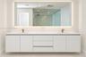 Floating white dual-sink vanity with a solid surface countertop, metallic finish faucets, a large rectangular mirror with integrated perimeter lightin