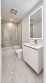 Bathroom featuring a floating vanity with a white countertop, wall-mounted illuminated mirror, porcelain tile flooring, and a glass-enclosed shower wi