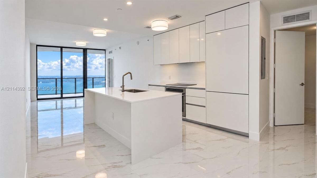 Modern kitchen featuring white flat-panel cabinetry, integrated appliances, a central island with a quartz countertop, and large-format porcelain tile
