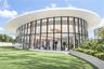 Elliptical glass-walled structure featuring floor-to-ceiling windows, a sweeping overhanging roofline, and integrated recessed lighting
